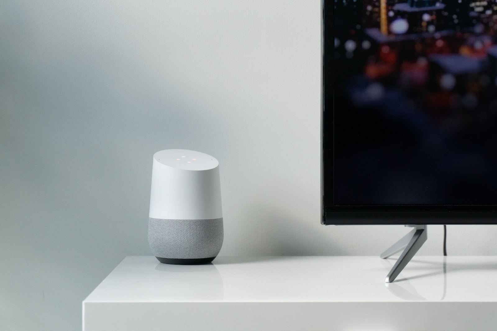 white and gray Google smart speaker beside black flat screen TV